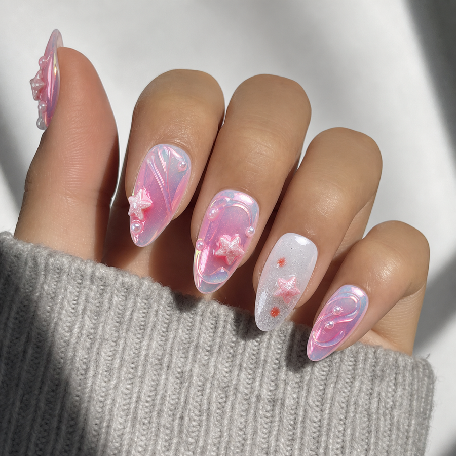 A close-up of a hand with long, glossy almond-shaped nails decorated in pastel pink and white marbled designs with small 3D floral accents, wearing a gray ribbed knit sleeve against a bright white background.